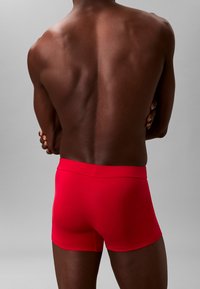 Bóxers de algodón rojos con un diseño ajustado y cintura elástica, vistos desde atrás sobre un fondo gris neutro.