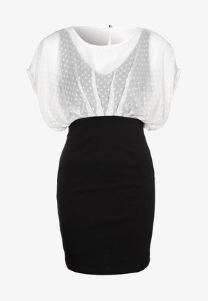 Robe noire ajustée avec un sur-blouse en tulle blanc à pois et un large décolleté en forme de goutte.
