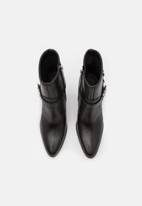 Czarne skórzane botki za kostkę z szpiczastym noskiem, zamkiem po boku i dekoracyjnym paskiem. Gładka faktura i smukły design.