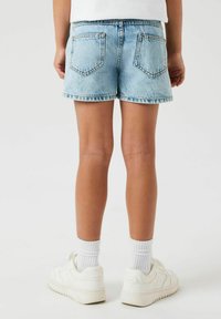 Jeans kratke hlače v svetlo modri barvi s strgano obrobo in dvema zadnjima žepoma. V kombinaciji z belimi supergami in rebrastimi belimi nogavicami, prikazano s hrbtne strani.