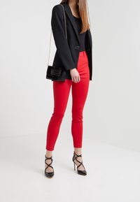 Zwarte getailleerde blazer, zwarte top, rode slim-fit broek en zwarte strappy hoge hakken. Zwarte gewatteerde handtas met kettingband.