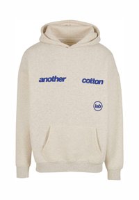 Felpa in cotone di colore beige chiaro con il testo blu "another" e "cotton", e logo circolare "lab" a sinistra. Caratterizzata da una tasca frontale e cappuccio con cordino.