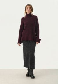 Bordeaux turtleneck trui met een losse pasvorm en brede manchetten, gecombineerd met een zwarte denimrok met een frontsplit en laarzen.