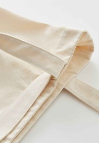 Katoenen draagtas in een natuurlijke beige kleur, met platte handvatten en een gladde textuur. Het ontwerp is eenvoudig zonder zichtbare patronen of hardware.