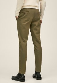 Olivgrüne Chinos mit schlanker Passform, flacher Vorderseite, zwei Gesäßtaschen und einem Knopfdetail, gefertigt aus einem glatten Baumwoll-Twill-Gewebe.