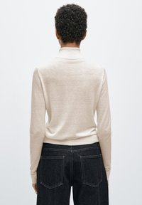 Gebreide beige trui met een hoge hals, lange mouwen en geribbelde boorden. Gecombineerd met donker denim jeans met twee achterzakken.
