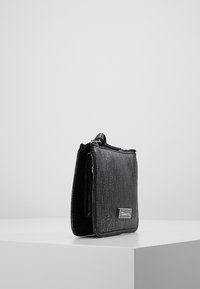 Svart texturerad läderhandväska med rektangulär form, utrustad med en silverfärgad logoplåt och en dragkedjestängning upptill.