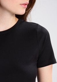 T-shirt noir à manches courtes en tissu lisse, avec un col rond classique et une coupe ajustée au niveau des épaules.