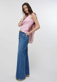 Haut rose sans manches associé à un jean en denim bleu à jambes larges. Le jean a une taille haute, des coutures visibles et une coupe décontractée.