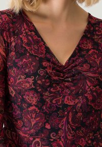 Mörkt, mönstrat linne med virvlande blommönster i rött, rosa och lila. V-ringning med samlad detalj vid bysten. Strukturerad tyg.