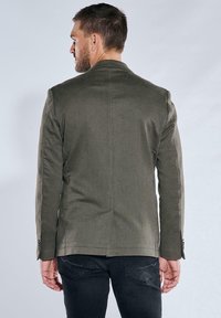 Maßgeschneiderte Jacke aus dunkelolivgrünem Stoff. Verfügt über einen einzelnen Schlitz und knöpfbare Manschetten, mit einer strukturierten Silhouette und glatter Textur.