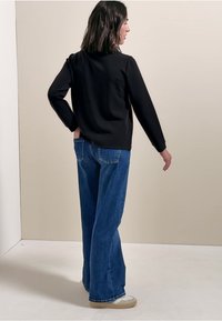 Zwarte top met lange mouwen gecombineerd met blauwe wijde jeans. De top heeft een gladde textuur en de jeans hebben achterzakken en een vervaagde wassing.