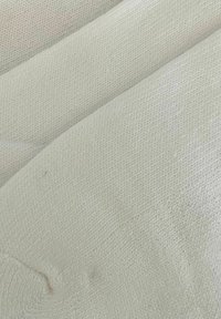Nahaufnahme von gefaltetem weißen Strickstoff, der die detaillierte Textur und das Muster des Materials zeigt.