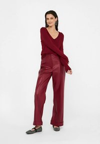 Bordó svetr s výstřihem do V a vysokým pasem bordó kalhoty z umělé kůže se širokými nohavicemi. Modelka má na sobě šedé vzorované baleríny.