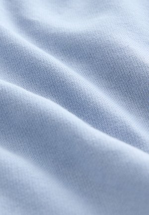 Világoskék szövet, puha, sima textúrával, finom kötött mintákkal és enyhe hajtásokkal, amelyek mélységet adnak a felületnek.