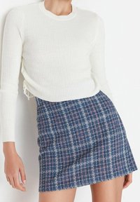 Haut blanc à manches longues côtelé associé à une mini-jupe à carreaux bleu marine avec des accents blancs et roses, mettant en valeur des tissus texturés.