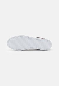 Semelle de sneaker blanche avec un motif de grip texturé, présentant une forme arrondie et un design minimaliste, adaptée à une utilisation décontractée.