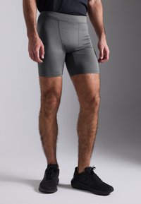Grå treningsshorts med tettsittende passform, glatt stoff, elastisk midjebånd og flate sømmer. Brukt med svarte treningssko.