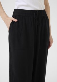 Pantaloni neri ampi realizzati in tessuto morbido, dotati di una vita elastica con coulisse, due tasche laterali e una forma rilassata.