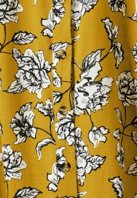 Tessuto giallo con stampa floreale nera, con grandi fiori e foglie. Cinque bottoni al centro, texture liscia.