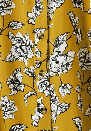 Gelber Stoff mit schwarzem Blumendruck, der große Blüten und Blätter zeigt. Fünf Knöpfe in der Mitte, glatte Textur.