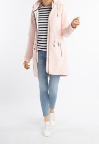 Personne portant un sweat à capuche zippé rose pâle avec cordons, un t-shirt rayé noir et blanc, un jean skinny bleu clair et des baskets blanches, marchant vers l'avant.