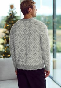 Grijze fuzzy trui met een ruitpatroon, ronde halslijn en ribbelzoom, gedragen met donkere broek, bekeken vanaf de achterkant.