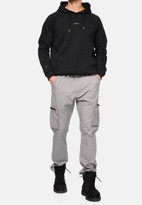 Sweat à capuche noir avec poche avant, pantalon cargo gris avec poches lat érales zippées, et bottes noires à lacets. Design simple et matériaux durables.