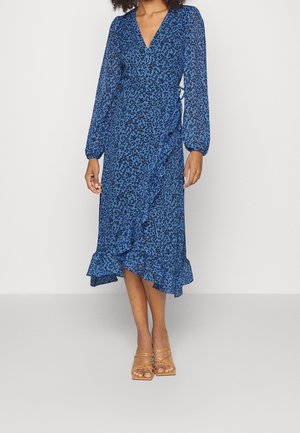 Niebieska sukienka kopertowa w kwiaty z długimi bufiastymi rękawami, falbaną na dole i głębokim dekoltem w kształcie litery V, wykonana z lekkiego materiału. Beżowe sandały na paski.