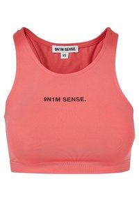 Korallfarget crop top laget av glatt, elastisk stoff, med rund utringning og svart trykt tekst "9N1M SENSE." foran.