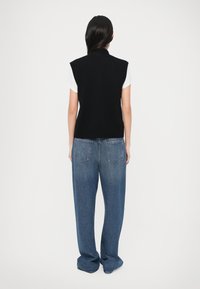 Top negro sin mangas de punto con cuello alto, combinado con vaqueros azules de corte holgado que cuentan con dos bolsillos traseros y un estilo relajado.