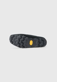 Black rubber sole with zigzag tread pattern, featuring a yellow Vibram logo. The upper section shows a textured, dark material.