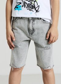 Graue Jeansshorts mit ausgefransten Säumen und Used-Details. Kombiniert mit einem weißen T-Shirt mit Aufdruck, zeigt einen lässigen Stil für Kinder.