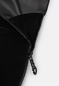 Interior de bolsa de ante negro, con forro de cuero y cremallera negra con un tirador decorativo en forma de cadena. Textura suave y diseñoMinimalista.