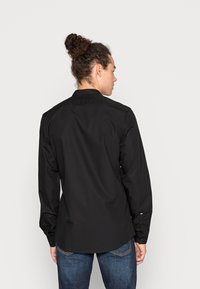 Camicia nera a maniche lunghe, con design button-down, colletto, tessuto morbido e orlo dritto. Indossata con jeans blu.