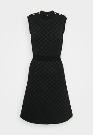 Sort ærmeløs strikket kjole med diamantquiltet mønster, ribbet taljebånd, høj halsudskæring og guldknapper på skuldrene.