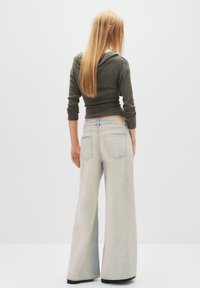 Hellblaue weit geschnittene Jeans mit einem ausgewaschenen Finish, kombiniert mit einem figurnahen, dunkelgrauen, gerippten Langarmoberteil mit Kapuze.