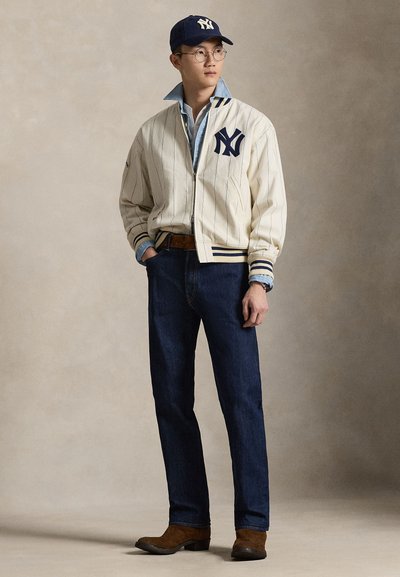 Valge triibuline pommirüü mereväe aktsentidega, sinine teksasärk, tumedad teksad ja pruunid saapad. Mehel on prillid ja ta kannab mereväe mütsi logoga.