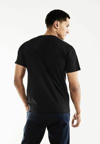 Černé bavlněné tričko s krátkým rukávem a kulatým výstřihem, s hladkým povrchem a minimalistickým designem, z pohledu zezadu.
