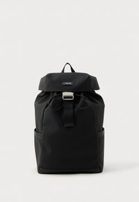 Juodas kuprinis krepšys, pagamintas iš tekstūruotos medžiagos, su užsegimu ant dangtelio, reguliuojamomis petnešomis, priekiniais sagtimis ir šoninėmis kišenėmis.