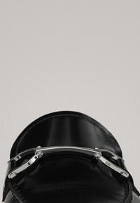 Chaussure en cuir noir au design élégant, avec une garniture en métal argenté incurvée sur le dessus, une texture polie et un bout arrondi.