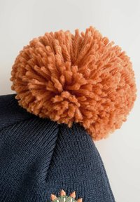 Dunkelblaue gestrickte Wintermütze mit einem großen, flauschigen orangen Pompon und einer teilweisen Sonnenstickerei am Rand.