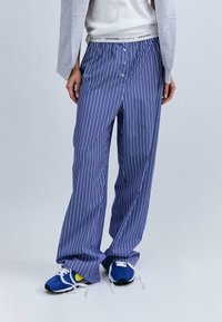 Pantalons de pyjama à rayures bleues et blanches, coupe décontractée, avec une braguette à boutons et une taille élastique arborant le logo de la marque. Tissu léger.