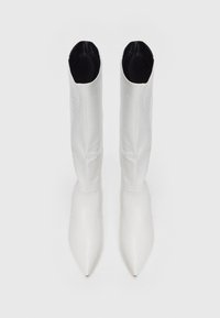 Botas blancas de rodilla con punta afilada, con un patrón texturizado de cocodrilo y forro interior negro, mostradas desde arriba sobre un fondo liso.