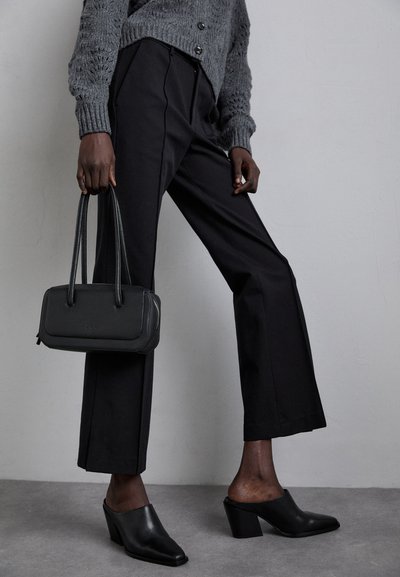 Black high-waisted trousers, gray knitted sweater, black heeled mules, and a structured black handbag with double handles.