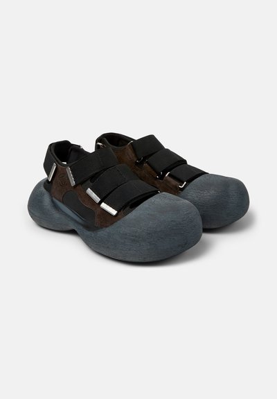 Chaussures marron épaisses avec de larges semelles arrondies grises et trois sangles noires réglables sur le dessus et à l'arrière.