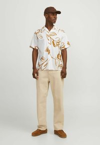 Camicia bianca a maniche corte con motivi floreali marroni, abbinata a pantaloni beige e scarpe marroni. Accessoriata con un cappellino marrone.