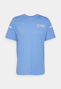 Camiseta de algodón de manga corta en azul claro. Presenta un estampado gráfico en una caja blanca en el pecho y detalles reflectantes en las mangas.