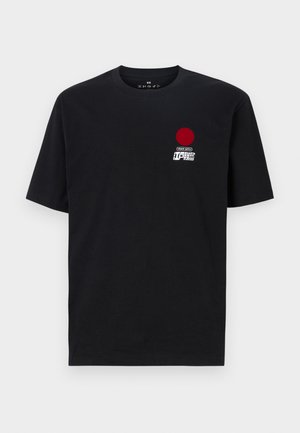 T-shirt en coton noir avec un graphique rond rouge sur la poitrine gauche, comportant du texte en blanc. Manches courtes et col rond.