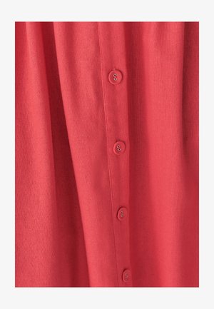 Koralfarvet skjorte med knapper, lavet af et tekstureret stof, der har en lodret række af seks knapper foran.